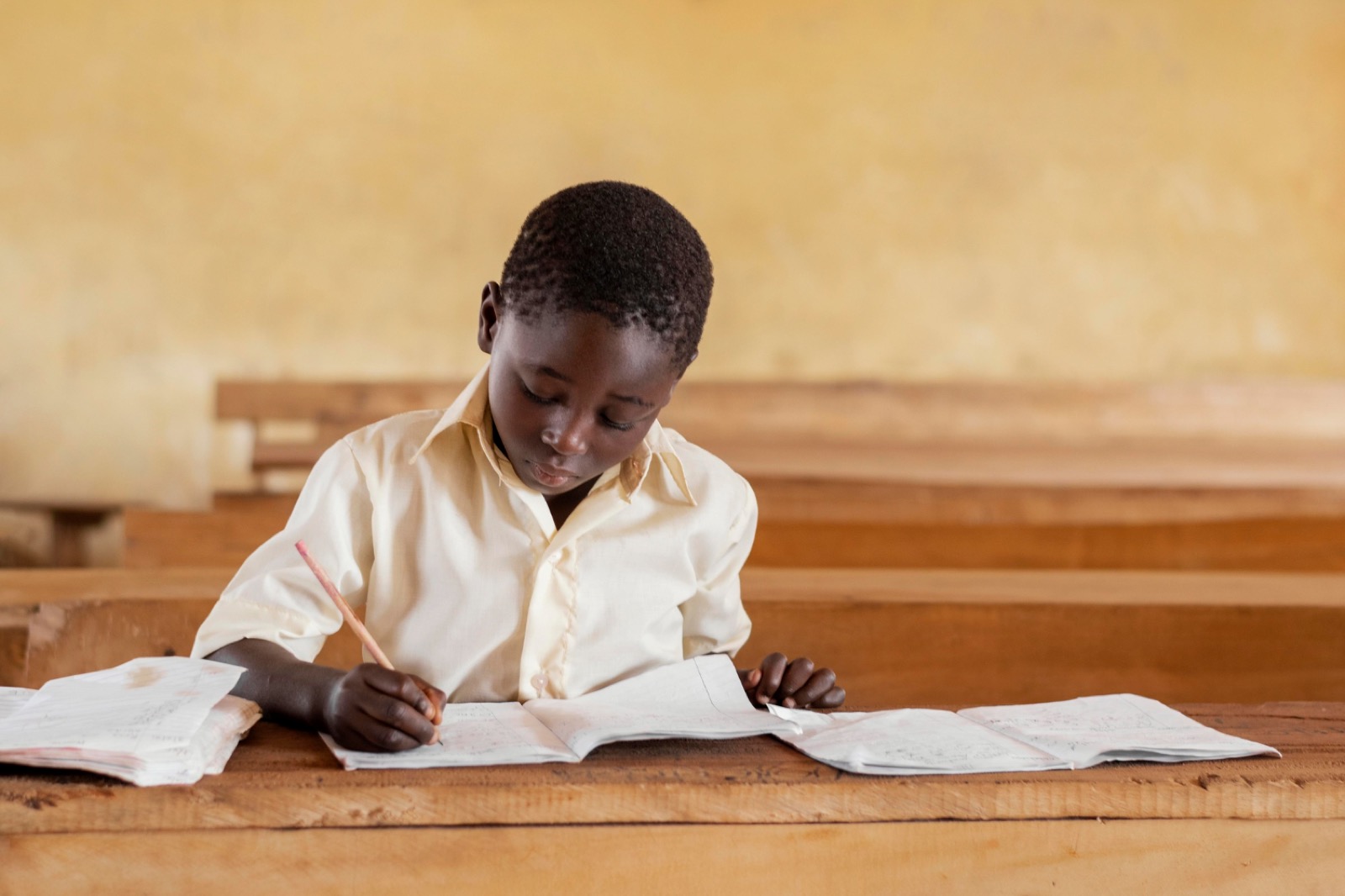 A pupil focused on her writing in a sunlit classroom