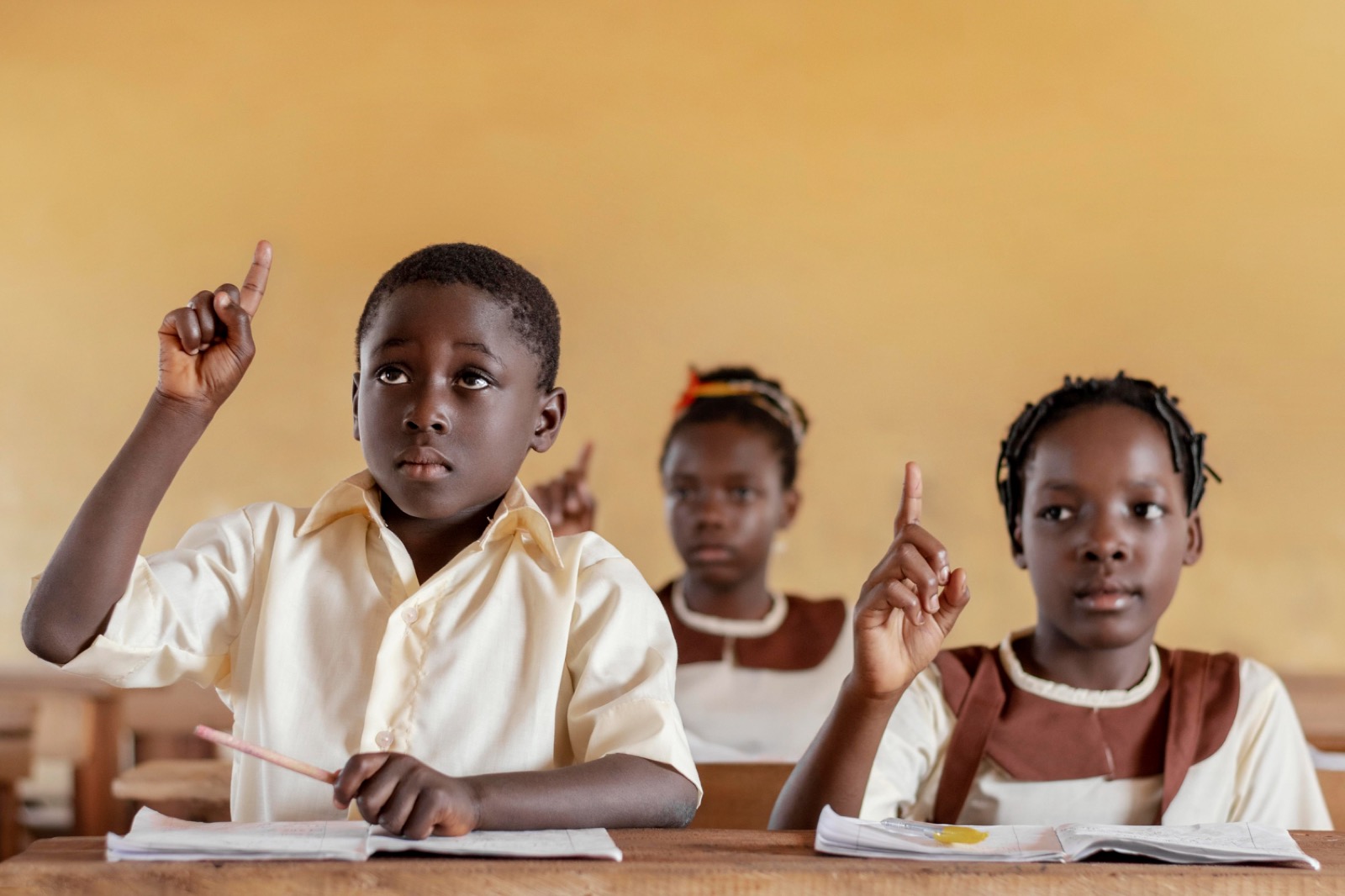 Three pupils raising their hands to answer in class